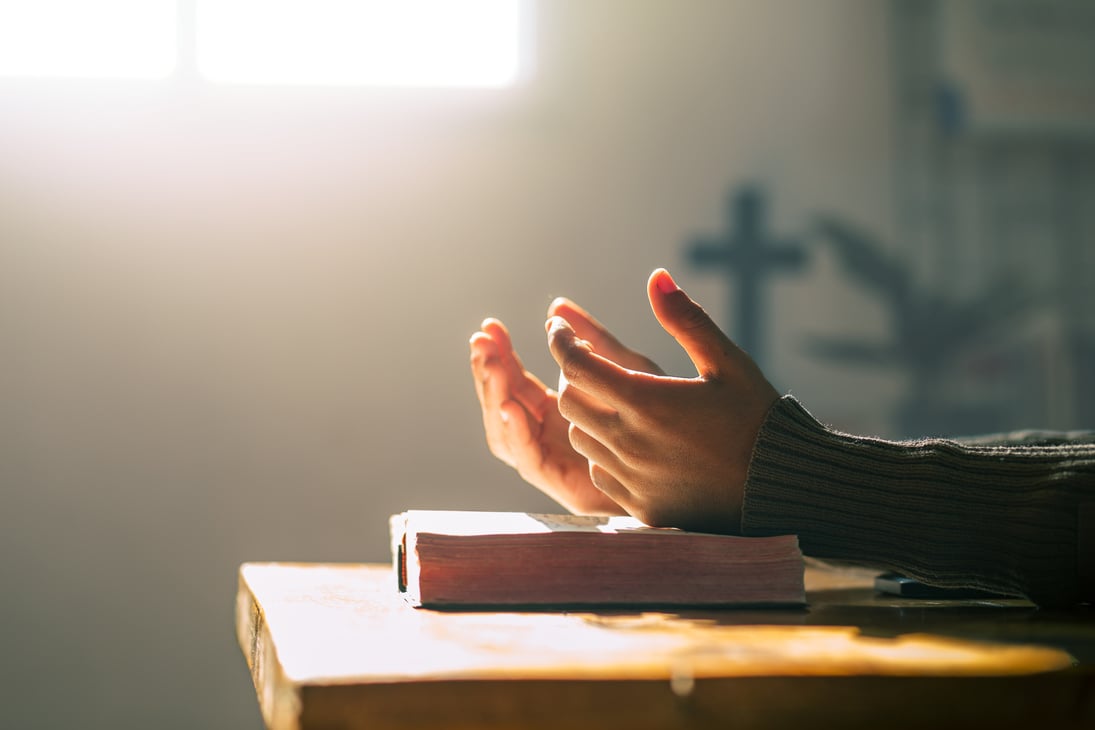 Christian pray to god. Holding hands in prayer with Bible on wooden table.